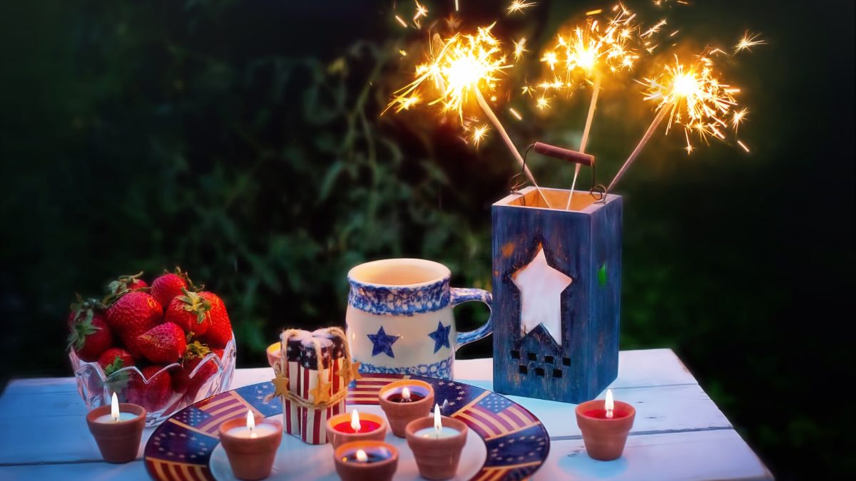 4th of July table setting with strawberries, festive candles, and sparklers in a blue vase.