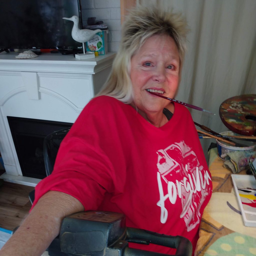 Dianne is sitting on her Amigo with a paintbrush in her mouth.