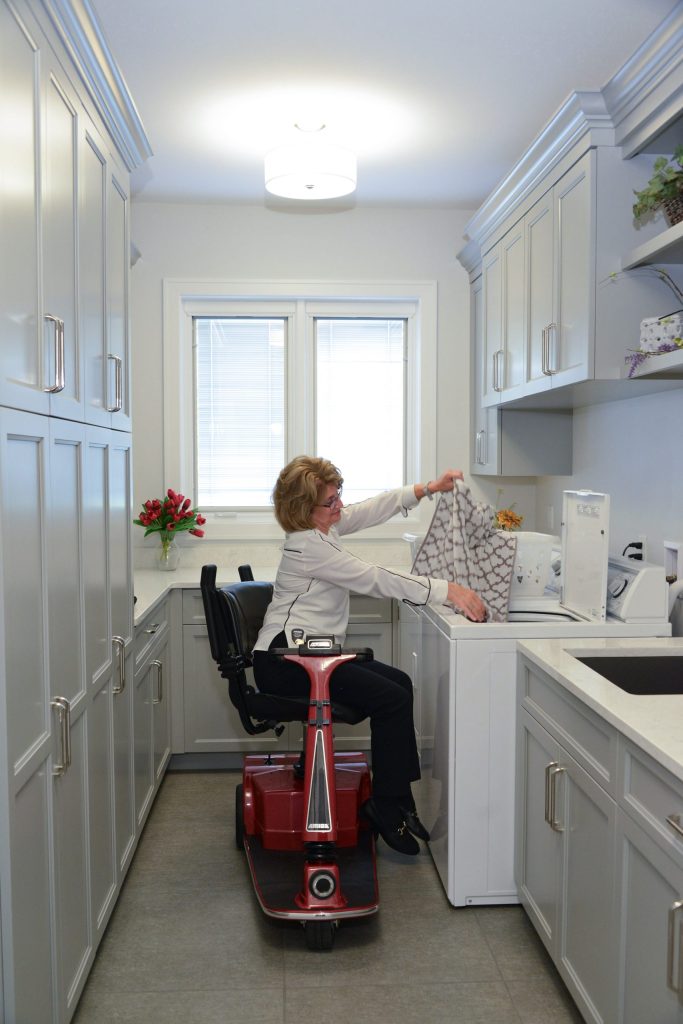 Woman seated on an Amigo scooter using the power seat lift while doing laundry.